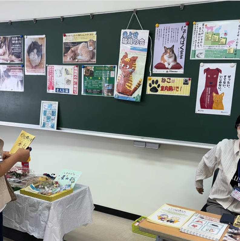 ふれあいまつりでの猫耳の会ブースの様子の写真。黒板にポスターが貼られているほか、チラシの配布やバザーが行われている様子が写っている